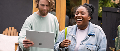 一位男士和一位女士拿着 Microsoft Surface 平板电脑大笑。
