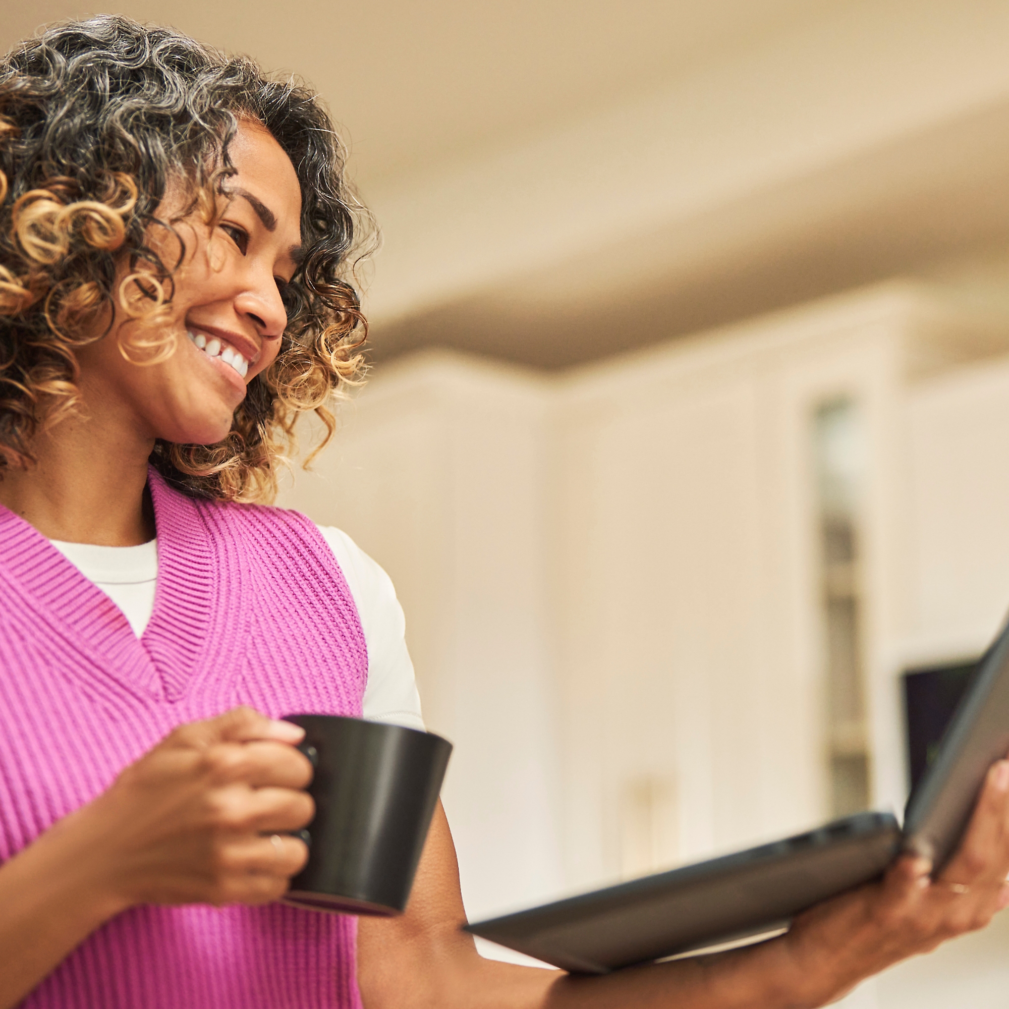 En kvinna ler med en kaffekopp i en hand och en bärbar dator i en annan